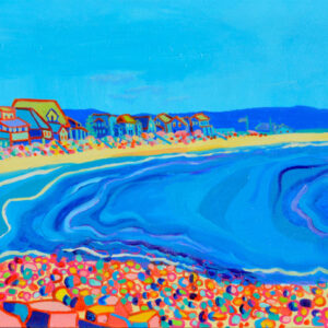 A beach scene on a bright, sunny day. The yellow sand pulls the viewer out along the length of the canvas dotted with cottages and brightly colored stones in the foreground. A hint of a sailboat is on the far right of the canvas, about to sail out of view.