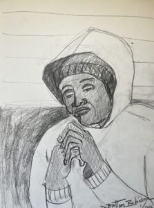 An African American lady sits at a cafe seat at Market Basket holding her hands. She wears a winter hat with the hood of her coat pulled up over the hat.